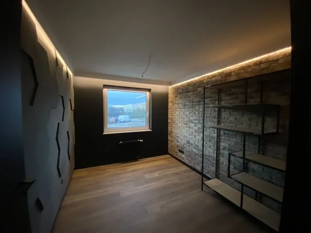 Ciemny salon z listwą LED, ścianą z cegły i metalowym regałem